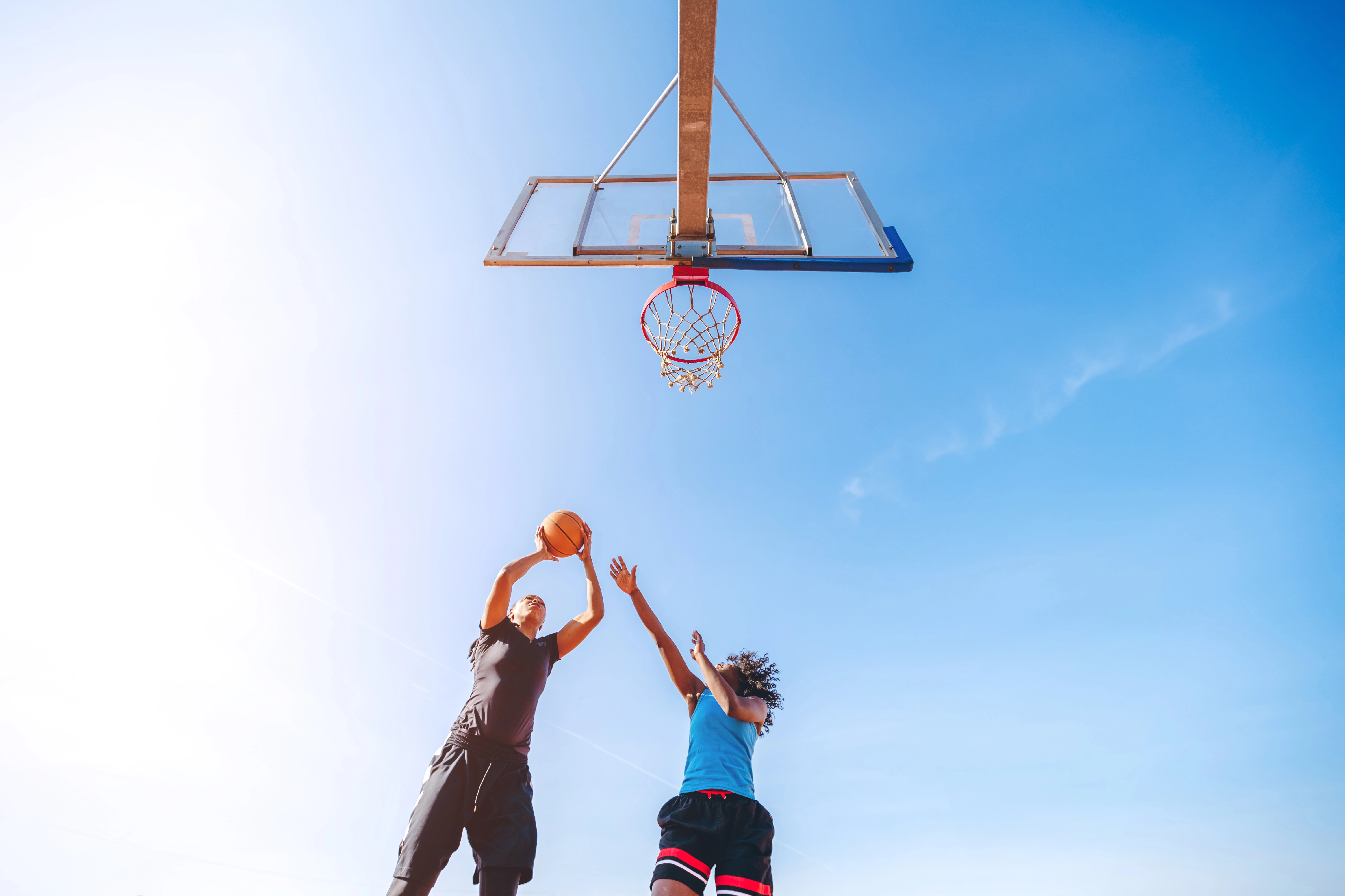 Two young women playing basketball, camera is looking up towards them as one of them is getting ready to shoot while the other defends.